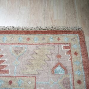 Terracotta, pink, and beige high-pile rug with geometric patterns and fringe on light wood floor.