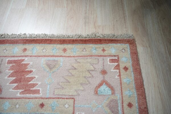 Terracotta, pink, and beige high-pile rug with geometric patterns and fringe on light wood floor.