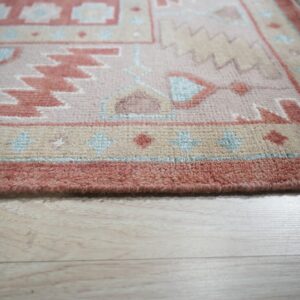 Geometric rug in dusty rose, cream, and light blue rests on light colored plank flooring.