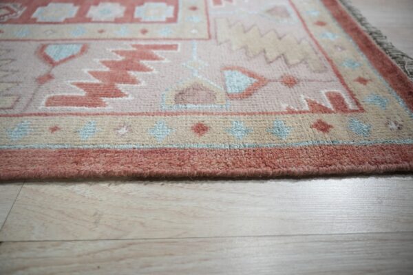 Geometric rug in dusty rose, cream, and light blue rests on light colored plank flooring.