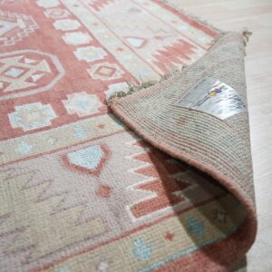 Geometric rose and cream rug with blue accents, curled up showing the backing on light wood floors.