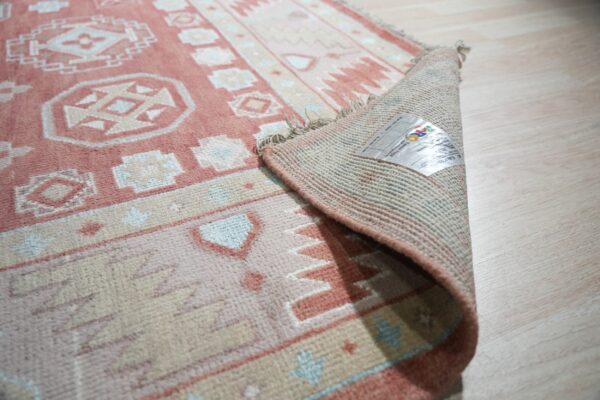Geometric rose and cream rug with blue accents, curled up showing the backing on light wood floors.