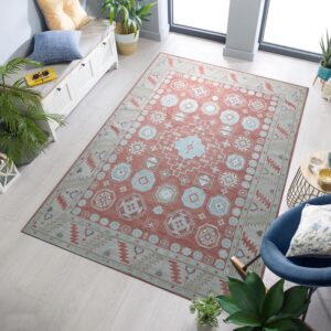 A terracotta and pale blue geometric rug sits on light wood floors beside a window and blue armchair.