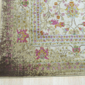 Distressed rug corner with cream, bright pink, yellow, and beige floral design on light wood floors.