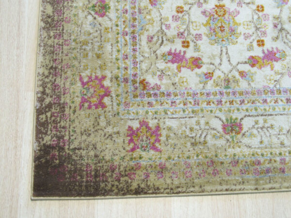 Distressed rug corner with cream, bright pink, yellow, and beige floral design on light wood floors.
