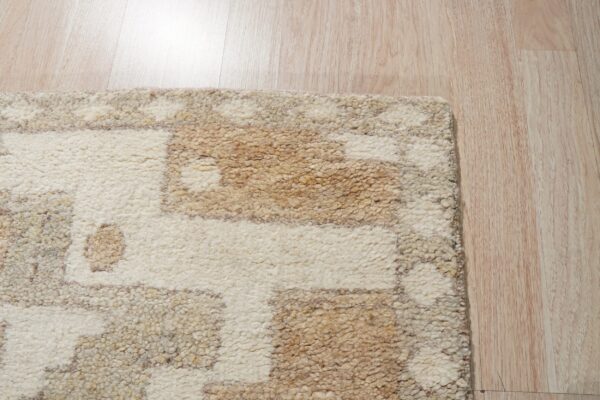 Shaggy cream and tan geometric rug corner shown on reflective, light blonde wood flooring.