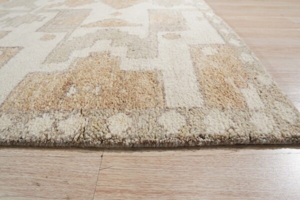 A close-up view of a shaggy cream and tan geometric rug on light plank flooring.