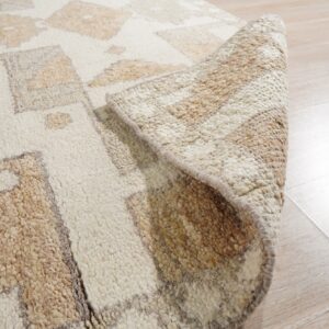 A thick, shaggy beige and cream geometric rug is partially rolled up on light wood flooring.