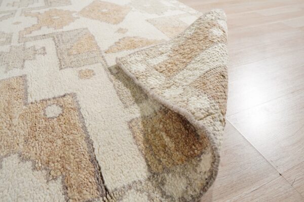 A thick, shaggy beige and cream geometric rug is partially rolled up on light wood flooring.