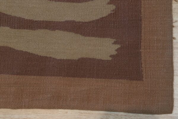 Flat-weave rug detail showing abstract brown and tan organic shapes and a solid border on wood flooring.