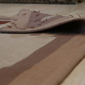 Beige, brown, and rust patterned low pile rug detail folded over a light wood floor.