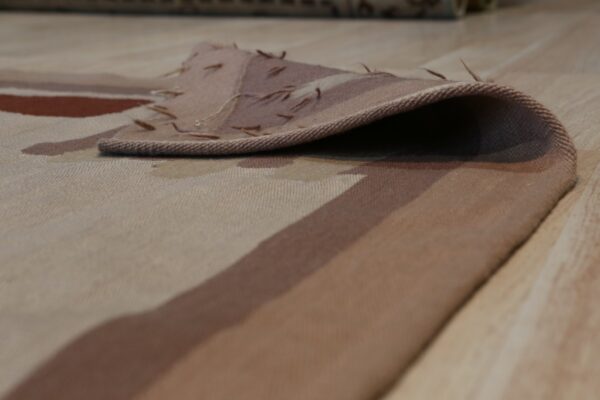 Beige, brown, and rust patterned low pile rug detail folded over a light wood floor.