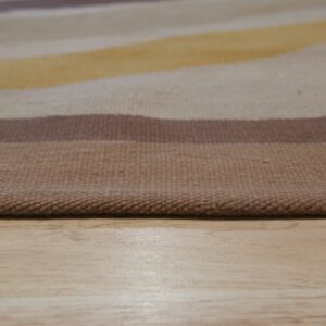 Low-angle product view of a striped flatweave rug in brown, yellow, and beige tones on light wood floor.