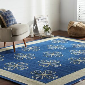 Blue area rug with repeating beige ornamental motifs and a thick border lies under a neutral armchair.