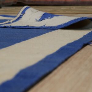 Low-angle view of a blue and cream striped low-pile rug edge folded over on wooden floorboards.