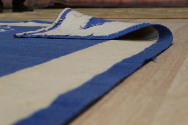 Low-angle view of a blue and cream striped low-pile rug edge folded over on wooden floorboards.