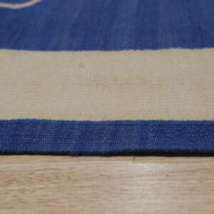 Close-up of a blue and cream low-pile rug edge resting directly on light wood flooring.