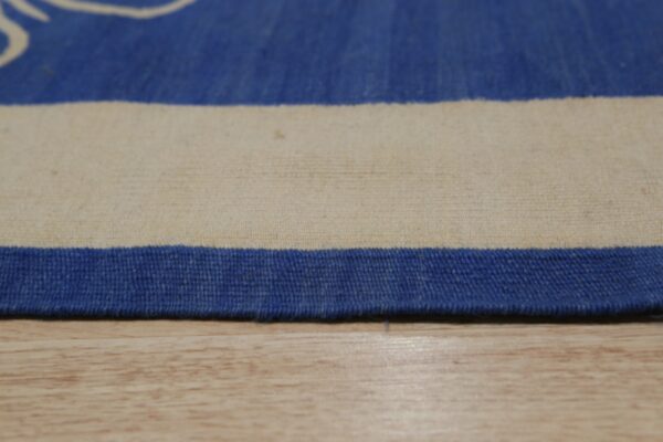 Close-up of a blue and cream low-pile rug edge resting directly on light wood flooring.
