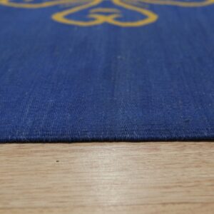 Low-angle view of a coarse, low-pile blue rug with yellow patterns resting on light wood flooring.