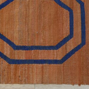 Rustic orange rug featuring a dark blue concentric octagonal geometric design on light wood floors.