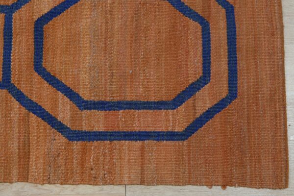 Rustic orange rug featuring a dark blue concentric octagonal geometric design on light wood floors.