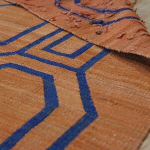 Detail shot of a flat-woven orange rug with bold blue geometric lines, folded over on wood flooring.