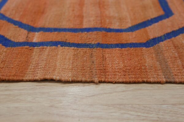 Flatweave rug detail in orange and blue geometric pattern resting on light wood flooring.