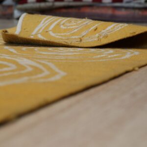 A golden-yellow rug with a white ring pattern is rolled back on light wood flooring.