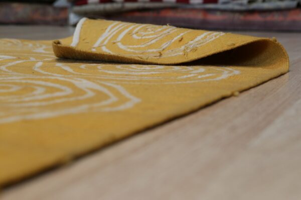 A golden-yellow rug with a white ring pattern is rolled back on light wood flooring.