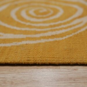 A flat-woven yellow and cream rug featuring a blurry spiral pattern rests on light wood.