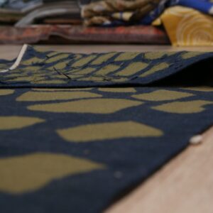 Low-pile rug in dark navy and olive green abstract pattern, folded on a light wood floor.