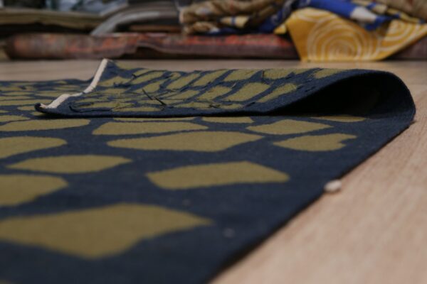 Low-pile rug in dark navy and olive green abstract pattern, folded on a light wood floor.