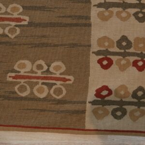 Brown and cream flatweave rug with geometric floral motifs resting on light wood flooring.
