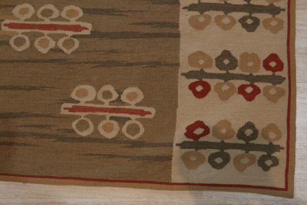 Brown and cream flatweave rug with geometric floral motifs resting on light wood flooring.