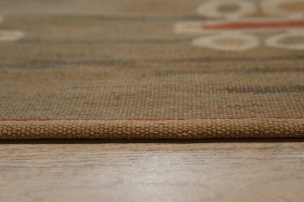Textured brown woven rug edge with a thin red line rests on light wood grain flooring.