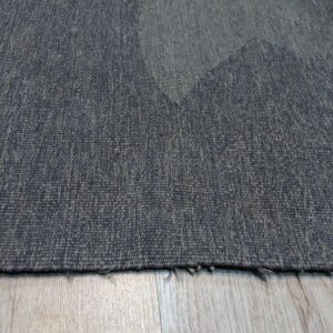 Textured, low-pile dark blue-gray rug with subtle geometric shapes lying on light wood plank flooring.