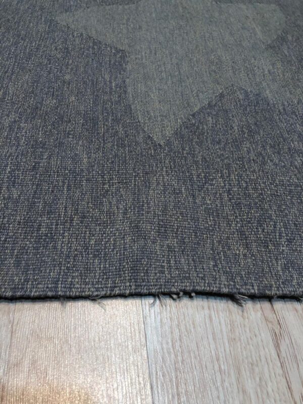 Textured, low-pile dark blue-gray rug with subtle geometric shapes lying on light wood plank flooring.
