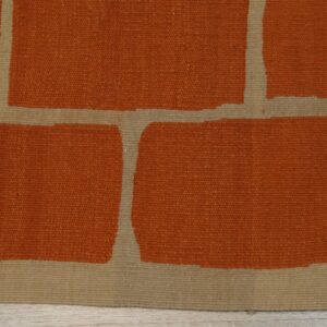 Rust and tan flatweave rug showing large block shapes on light wood plank flooring.