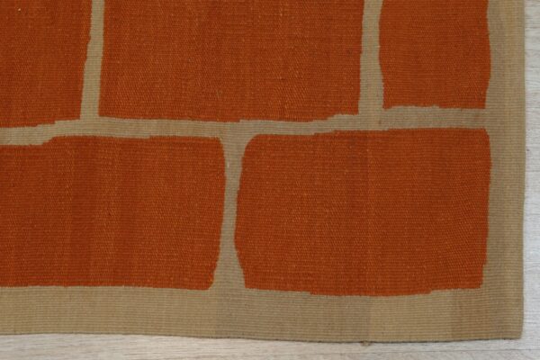 Rust and tan flatweave rug showing large block shapes on light wood plank flooring.