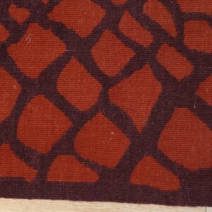 Flat weave rug featuring a rust orange abstract pattern framed by dark maroon lines over light wood flooring.