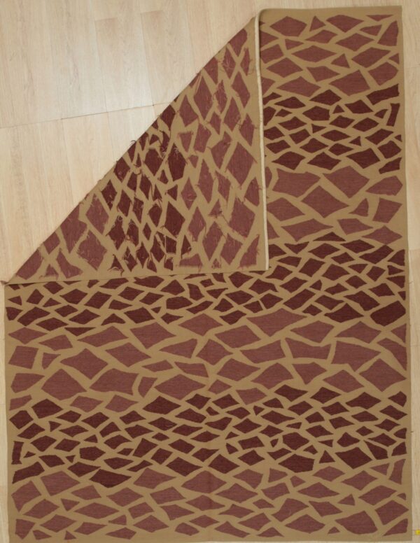 Tan flatwoven rug with dark brown abstract diamond shapes, displayed folded on light wood flooring.