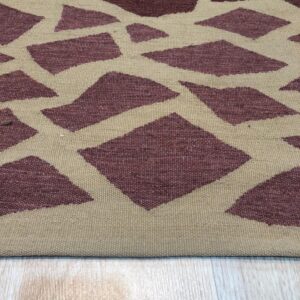 A tan flatweave rug features an irregular burgundy pattern of diamonds and triangles on a pale wood floor.