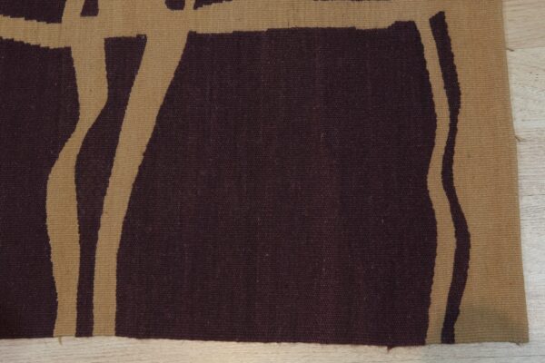Close-up of a flatweave rug with abstract burgundy and tan stripes on light wood flooring.