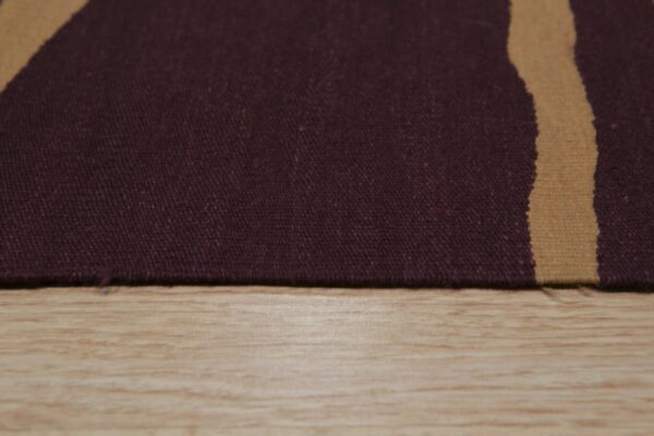 Close-up of a tightly woven, deep burgundy rug with a single tan stripe against light wooden flooring.