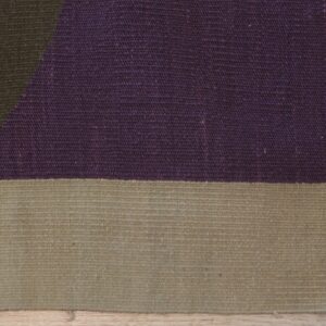 Flat-weave rug close-up showing purple and tan blocks with a dark green diagonal pattern on wood floor.
