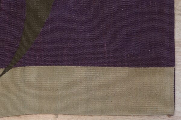 Flat-weave rug close-up showing purple and tan blocks with a dark green diagonal pattern on wood floor.