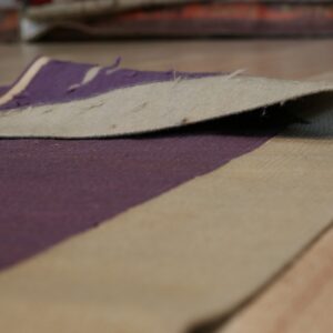Close-up showing the curled edge of a purple and beige rug on a light wood floor.