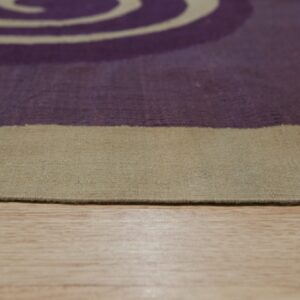 Low-angle view of a low-pile rug featuring a beige border and purple pattern on wood floor.
