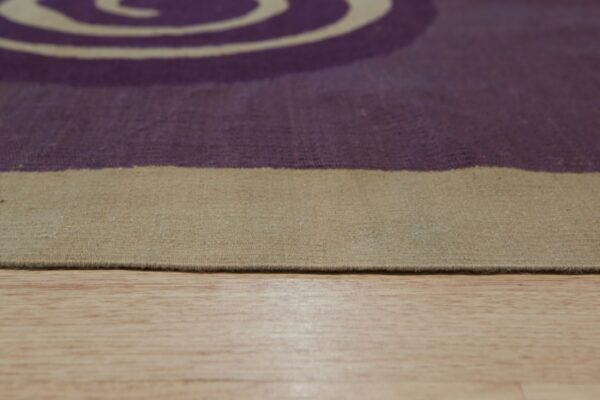 Low-angle view of a low-pile rug featuring a beige border and purple pattern on wood floor.