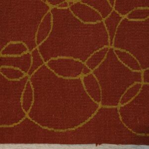 Detail view of a low-pile rust rug featuring interlocking yellow-green circles on light wood flooring.